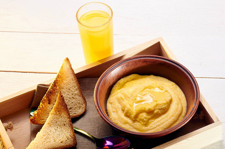 玉米粥配黄油和一些脆面包。橙色的新鲜榨汁和食物放在盘子里, 在床上吃早饭。在工作前的清晨简单可口的食物