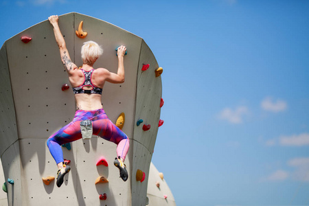 照片从年轻运动员的背部与短发型在墙上攀岩反对蓝天的女子