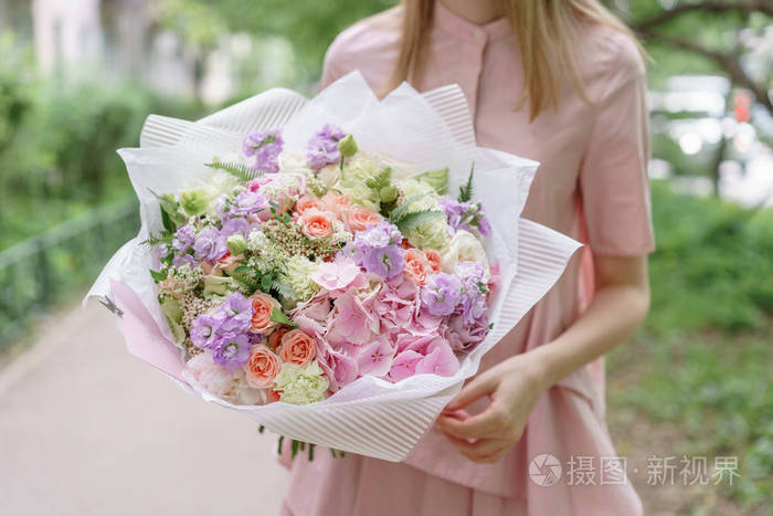 年轻女孩捧着美丽的夏日花束.花的安排与绣球和牡丹.花店的概念.