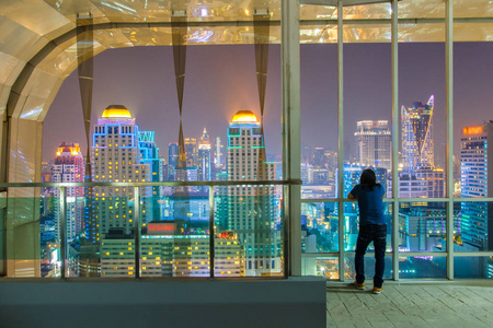 亚洲年轻人独自站在晚上的时间看看窗外的视图曼谷市