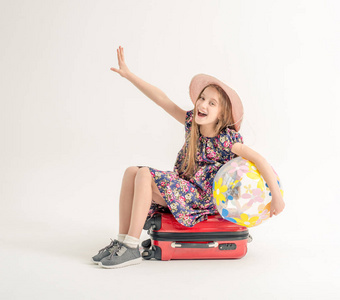快乐的小女孩正坐在一个手提箱和一个球