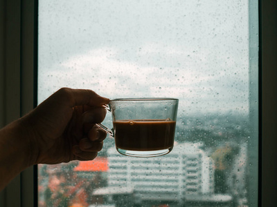 手捧一杯热咖啡在雨中滴窗