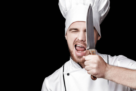 年轻人有胡子的人穿白色制服的厨师在黑色背景上持有当着面刀