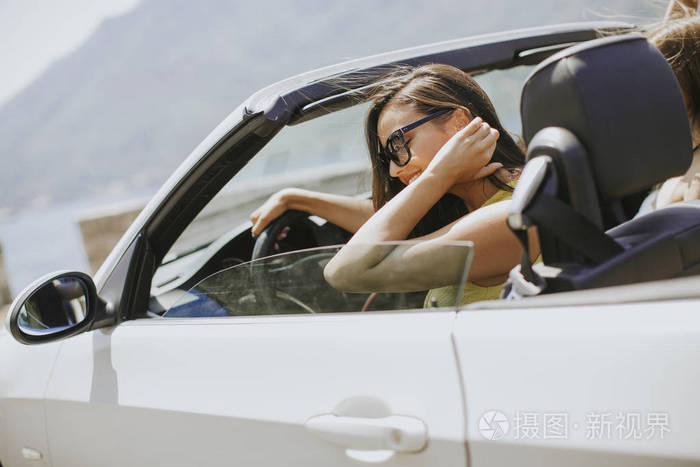 戴墨镜的年轻女子驾驶着她的敞篷车, 在晴朗的阳光明媚的天近海