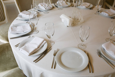 圆桌上覆盖着白色桌布盘子眼镜和餐具。