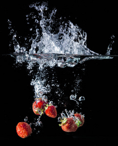 草莓在水中洒下, 鲜红的浆果。黑色背景
