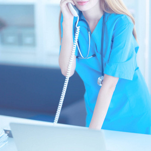 年轻的女医生穿白色上衣，在计算机上使用电话