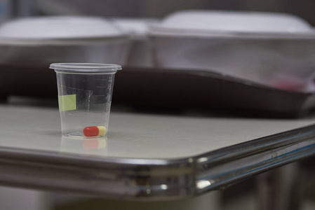 一个黄色橙色胶囊的药物在塑料杯在托盘上。住院病人膳食背景