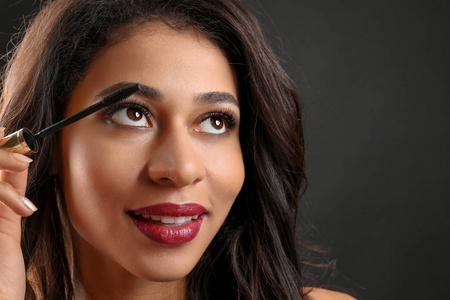 有吸引力的非洲裔美国妇女与长睫毛使用睫毛膏在黑色背景。睫毛延长