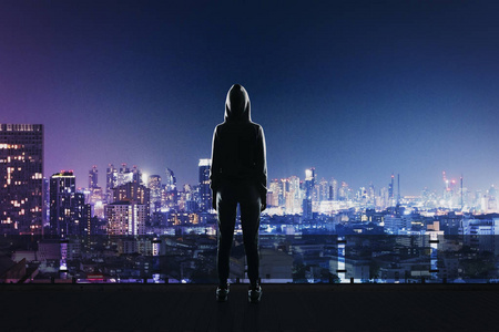 反观的黑客在运动西装站在屋顶上的夜晚同义词市照片
