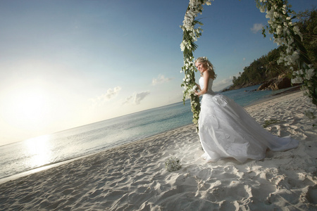 华丽的新娘笑着，站在太阳下婚礼拱