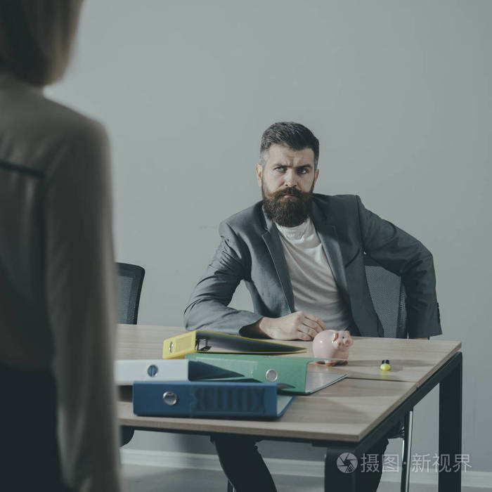 严肃的老板看着前景模糊的女人.留胡子的人坐在桌子上的办公室.