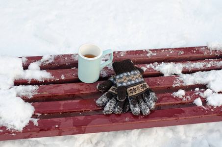 蓝杯子茶和妇女的针织的手套在冬季，雪在后台的长凳上。特写