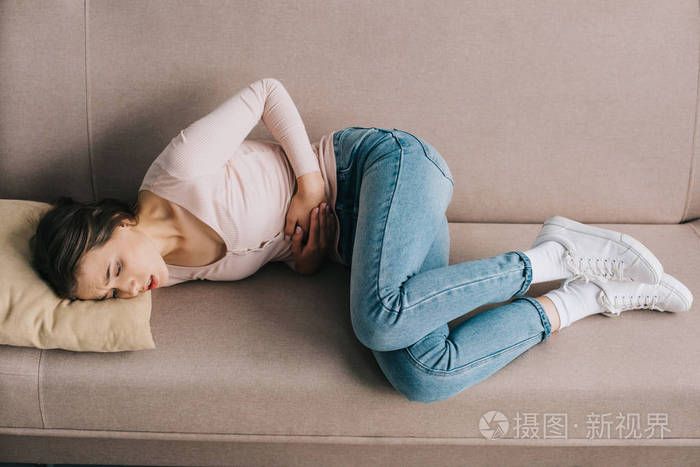 家庭沙发上躺在肚子痛的年轻妇女的高角度观
