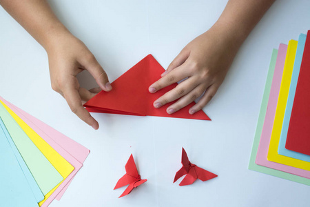 儿童的手做折纸蝴蝶从彩色纸在白色背景。折纸蝴蝶课