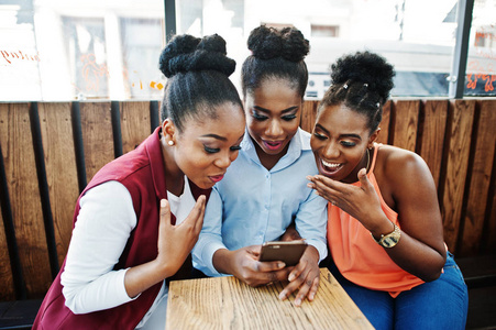 三位非洲裔美国女孩坐在咖啡桌上, 看着手机