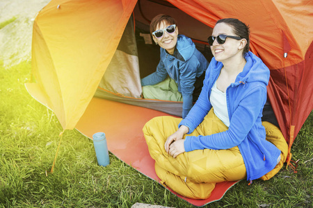 女孩坐在一个帐篷一个露营地附近河禁令