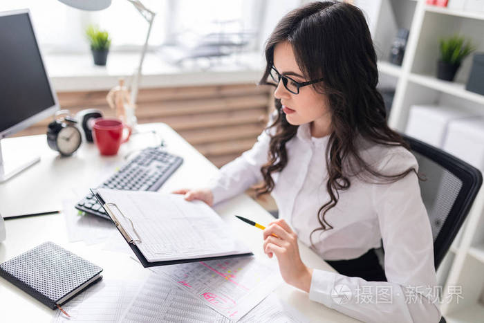 一个年轻的女孩坐在办公室的办公桌前检查文件