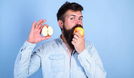 人胡子吃果子, 持有苹果蓝色背景。一半的苹果健康的生活方式。营养价值观念。保健节食维生素营养。时髦展示自然生态苹果