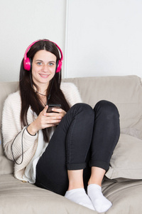 美丽的女孩在家庭沙发上粉红色耳机听音乐