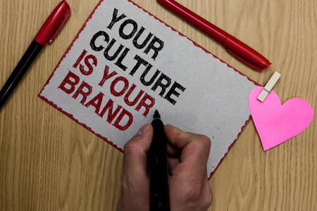 显示您的文化的文字符号是您的品牌。概念照片知识体验是一个演示卡写粘纸条夹捏心脏手拿着标记红色钢笔在木桌上