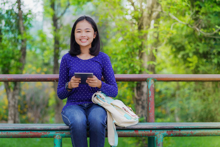 在阳光明媚的夏日, 在公园里使用数码平板电脑的亚洲学生女孩