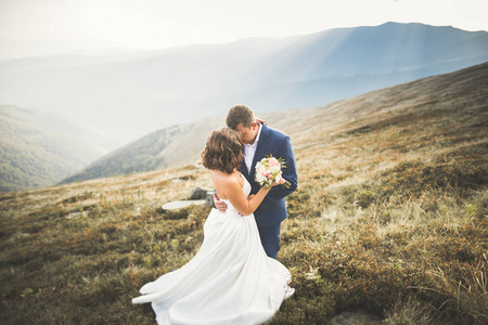 快乐的美丽婚礼夫妇新娘和新郎在婚礼当天在户外在山的岩石。幸福的婚姻夫妇在户外对自然，柔和的阳光灿烂灯光