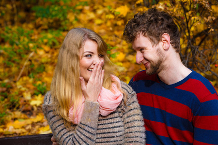 秋天的概念爱团结和关系。年轻的情侣坐上板凳在秋天公园中拥抱阳光明媚的日子