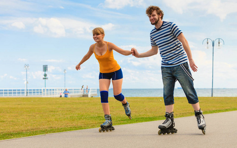 假日 活跃的人和友情观。年轻人适合溜冰鞋户外骑大海岸边，女人和男人滑旱冰一起长廊上的一对