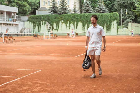 老式网球运动员在网球场训练后步行带袋
