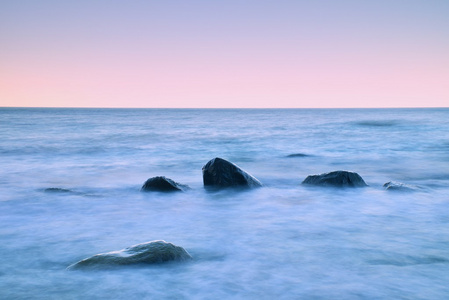 在海上的浪漫早晨。坚持从光滑水位的巨砾。与第一个炎热的太阳光线的粉红色 horozon