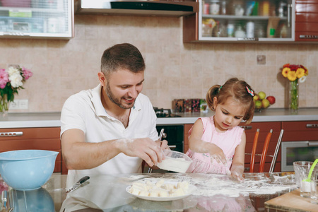 小女孩帮助男人煮懒饺子在餐桌上洒面粉。快乐的家庭爸爸, 孩子的女儿在周末早上在家里做饭。父亲节假期。育儿童年概念