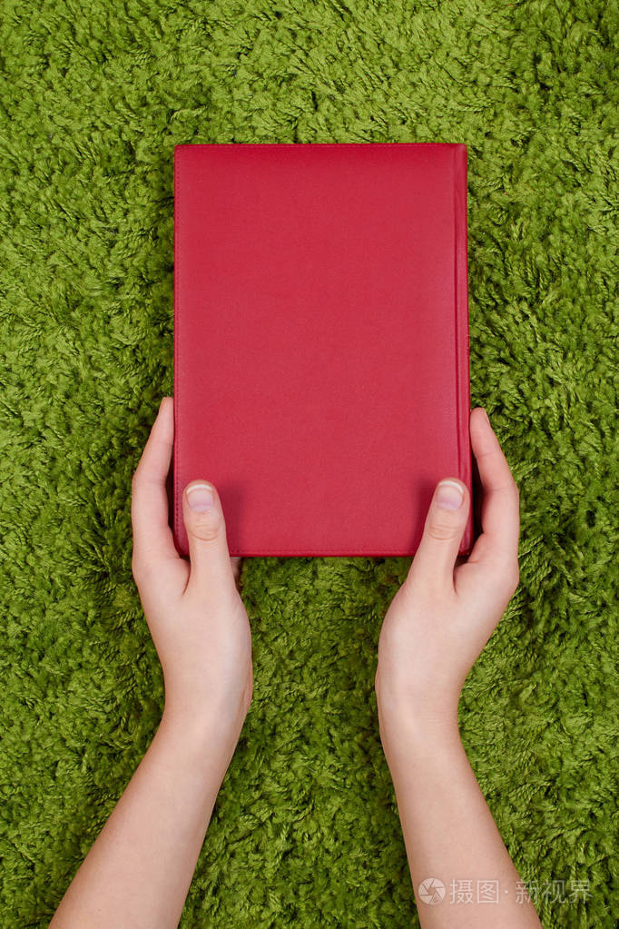 女人的张开双手捧着一本书,绿色背景上孤立手势保护