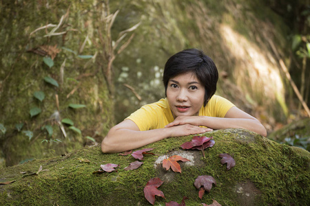 一个漂亮的亚洲女孩的肖像与干燥的红黄枫叶在石头上举行