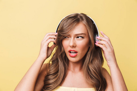 失望的白种女人20s 的照片, 长棕色的头发表达愤怒和厌恶, 而听音乐通过耳机隔离在黄色背景