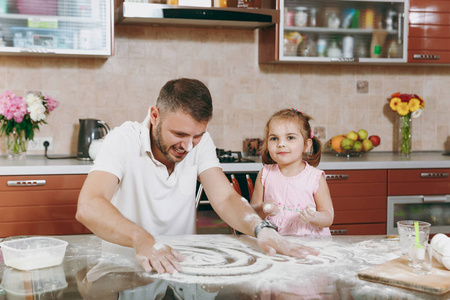 小女孩和男人玩耍, 在厨房的餐桌上画上散落的面粉。快乐的家庭爸爸, 孩子的女儿做饭, 周末早上的饼干。父亲节假期。亲子童年