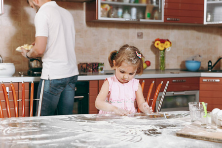 小女孩玩面粉, 而爸爸在厨房做饭在餐桌上。幸福的家庭爸爸, 孩子的女儿做饭, 周末早上在家里吃饼干。父亲节假期。亲子童年