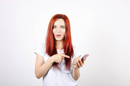 年轻漂亮的红头女子微笑着指着食指在空白屏幕智能手机。有吸引力的女性显示手机手机显示屏。独立背景, 复制空间, 背景, 特写