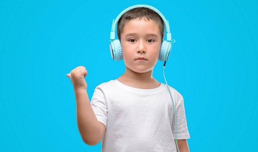 黑发小孩子听音乐用耳机指向用手和手指与愉快的面孔微笑