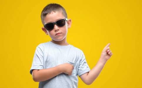 深色头发的小孩戴着太阳镜非常高兴地用手和手指指向侧面