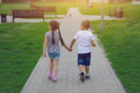 孩子们, 一个男孩和一个女孩在阳光明媚的日子里沿着人行道散步。后退视图