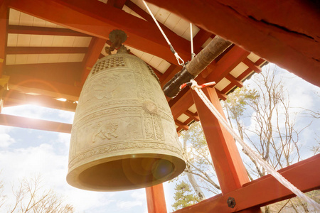 大黄铜佛教钟和日本寺庙的木材敲在明亮的蓝天与太阳和透镜光晕背景的红色亭子