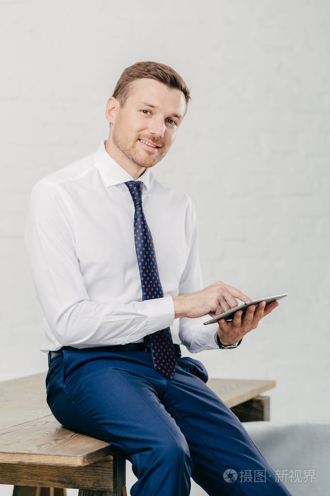 微笑的年轻商人在优雅的衣服高兴地收到收入信息, 在现代平板电脑, 坐