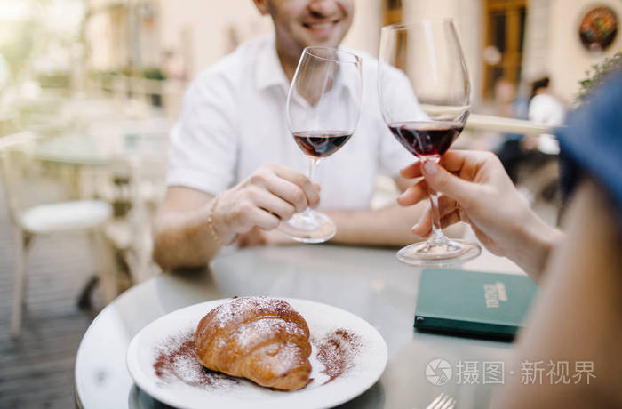 干杯.一对年轻的情侣坐在一起, 微笑着, 举杯与两个红酒酒杯