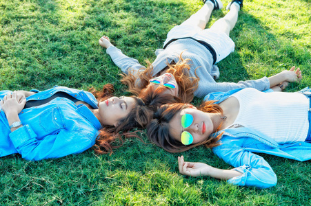 三个亚洲快乐女孩躺在绿草中的太阳镜