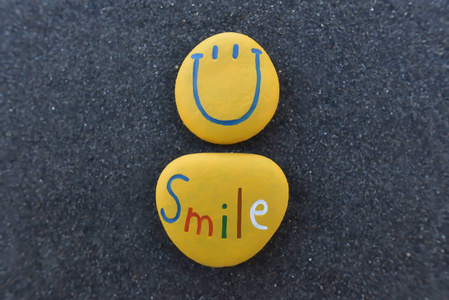 快乐的笑脸图释设计用彩色石头在黑色的沙