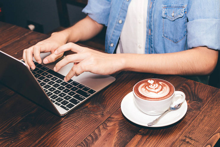 咖啡店的妇女喝咖啡和工作在笔记本电脑上