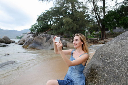 在海边的空海滩上用智能手机制作自拍的年轻女孩