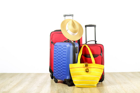 三个手提箱, 红色纺织品和蓝色硬壳行李, 扩展伸缩手柄, 草帽, 沙滩袋, 镜像太阳镜, 白色墙壁背景。情侣撤退旅行的概念。关闭