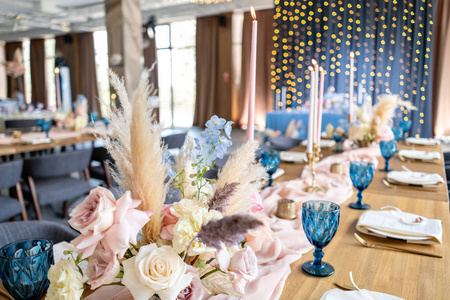 餐厅的豪华晚宴。美丽而精致的婚礼庆典装饰。宴会桌上有米色的粉红色桌布盘子和烛台和蜡烛。